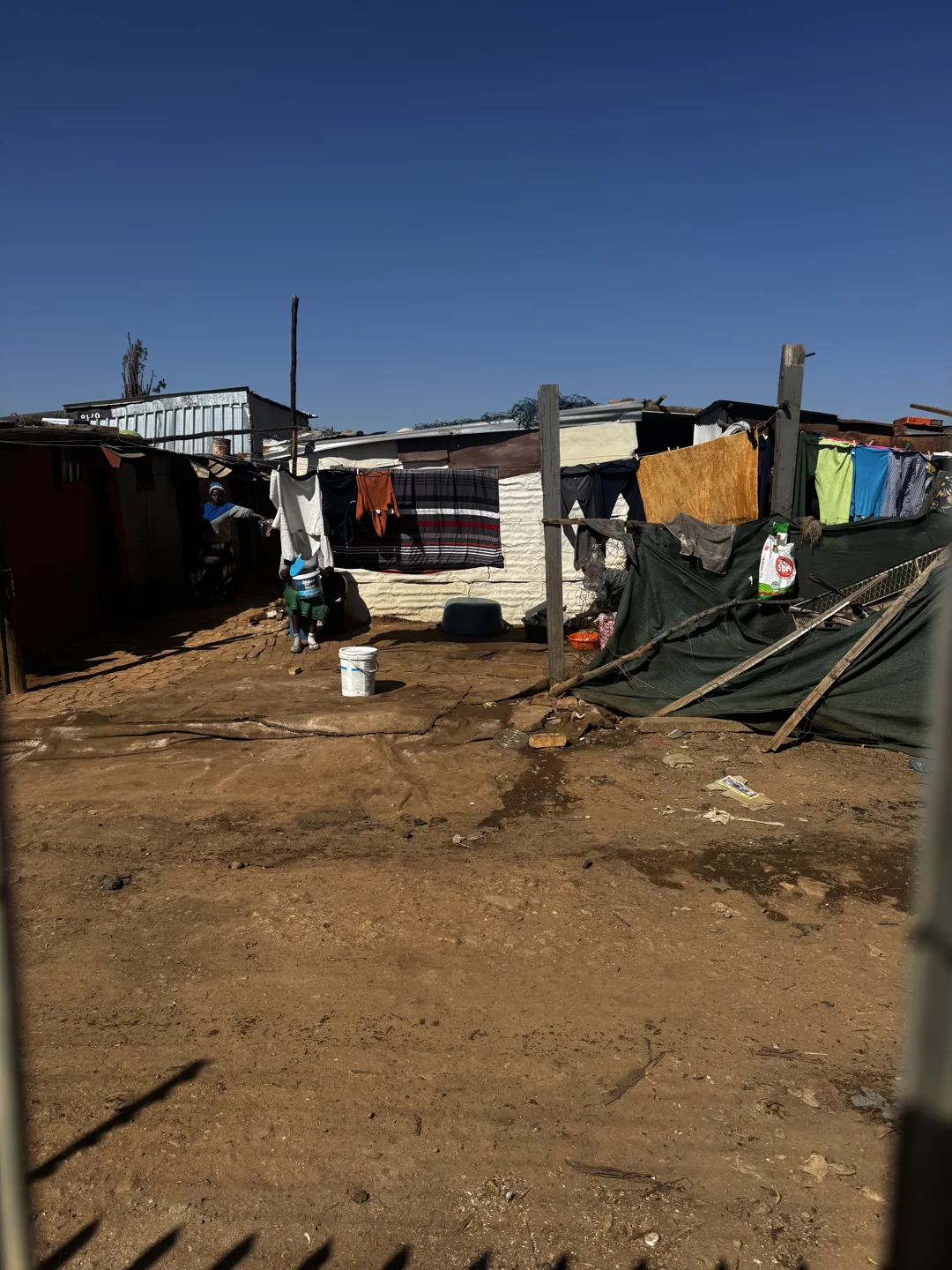 Informal dwellings with corrugated roofs beside a dirt path in Moreleta Park.